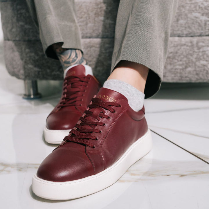 Maroon sneakers with white soles worn by a person sitting on a couch.